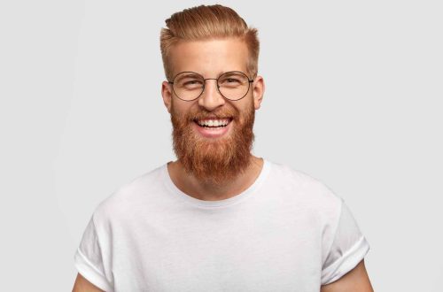 People, youth, positiveness concept. Happy male with long thick ginger beard, has friendly smile, rejoices having day off for his hobby, expresses happiness, stands alone against white wall.